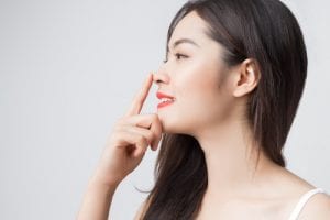 Young beautiful Asian woman with smiley face and red lips touching her nose